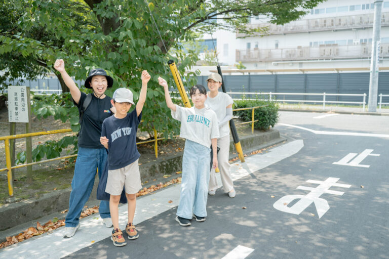リアル教室の近くで、手を上げて並ぶ教室長と子どもたち
